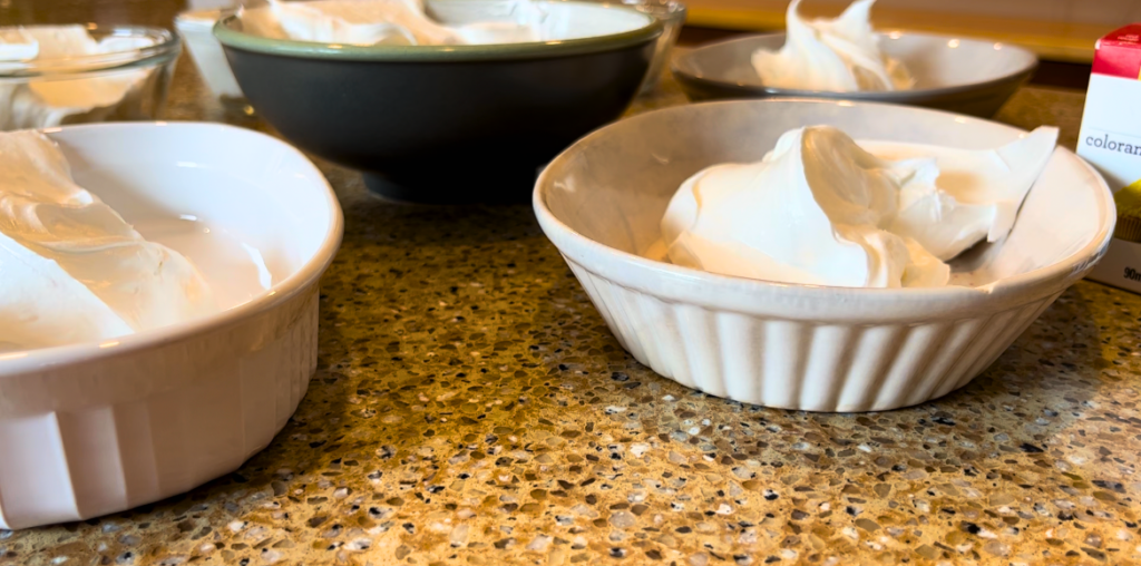 Royal icing separated into bowls on a brown countertop