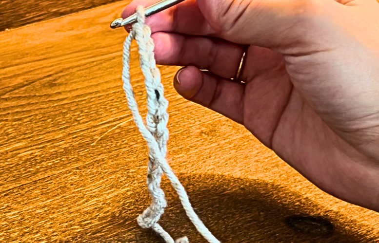 woman making a chain stitch with grey yarn
