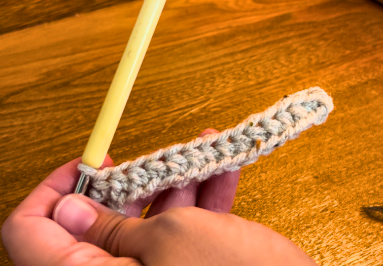 Woman showing a row of half double crochet stitches with grey yarn