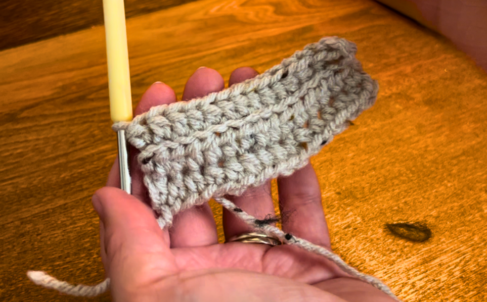 woman showing two rows of half double crochet in back loops only, with grey yarn.