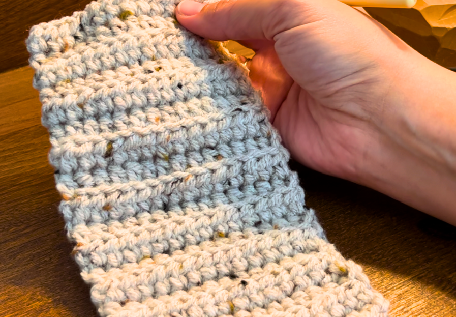 A woman holding a cuff made from half double crochets in back loops only, with grey yarn