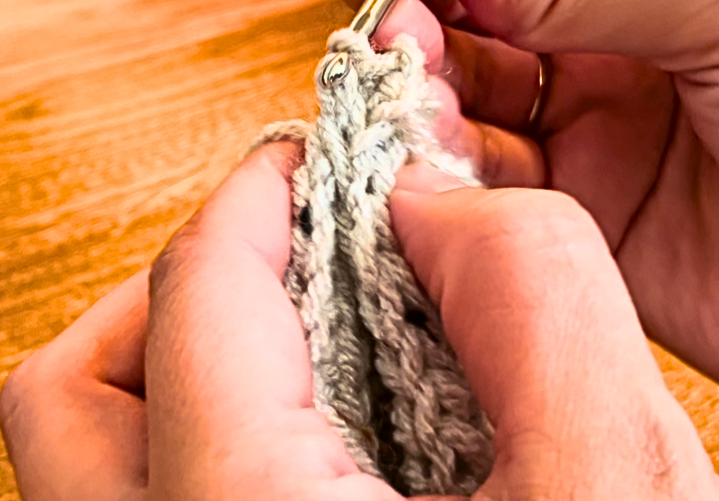 Woman joining to ends of crochet fabric together to make a cuff, in grey yarn