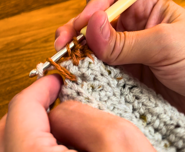 Woman crocheting half double crochets on top of the grey cuff in pheasant