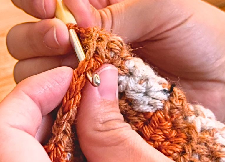 Woman making a slip stitch to join the thumb hole of the gloves