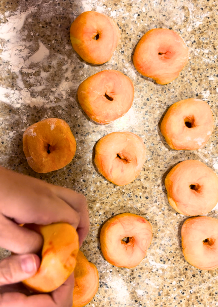 woman placing holes in the centre of the orange dough balls