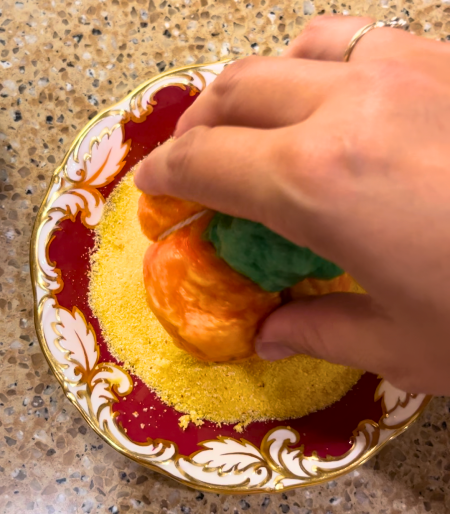 Woman dipping bagel dough onto a plate with cornmeal