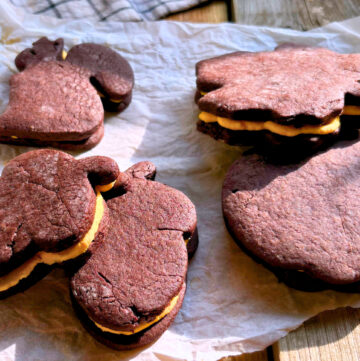 Chocolate sandwich cookies with orange icing sitting on a piece of parchment paper