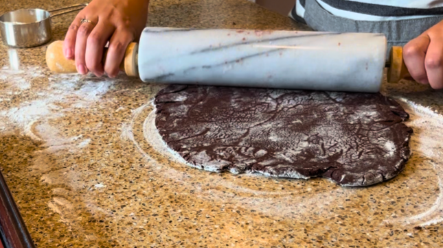 Woman rolling out chocolate cookie dough with a marble rolling pin