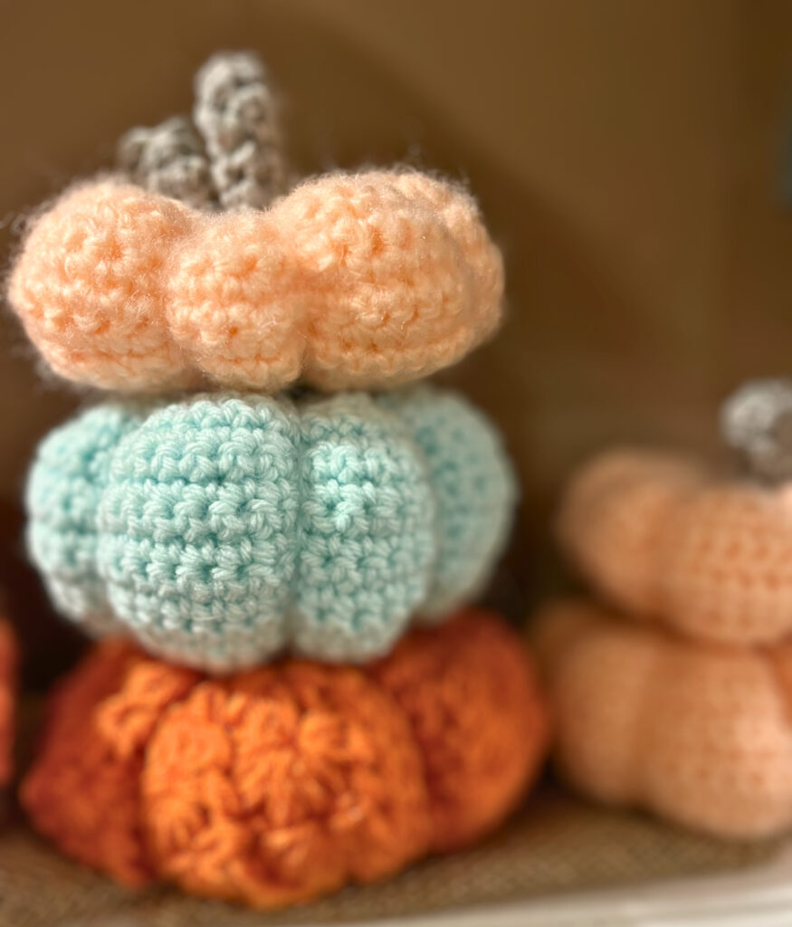 Stacked crochet pumpkins in orange, blue and peach.