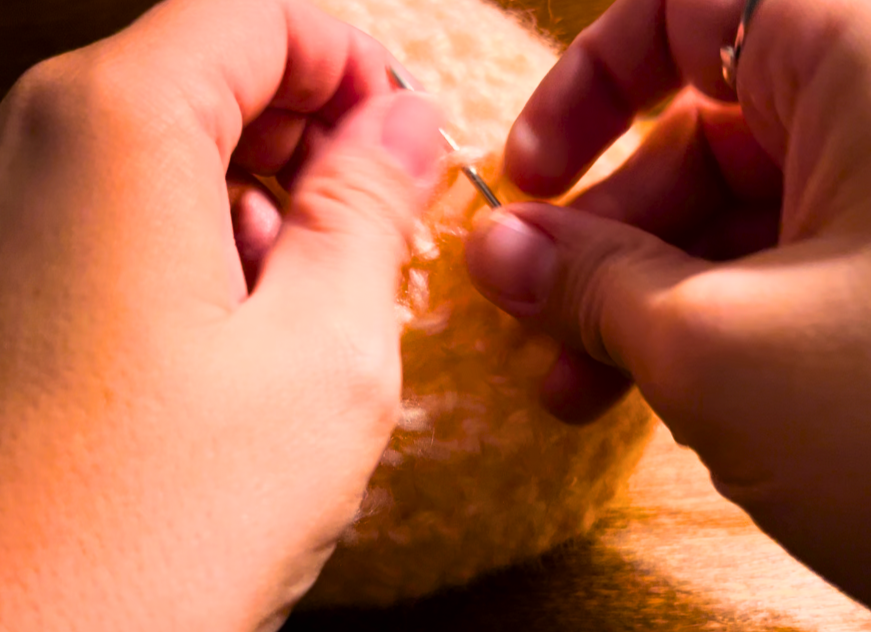 Woman sewing a crochet pumpkin with a darning needle