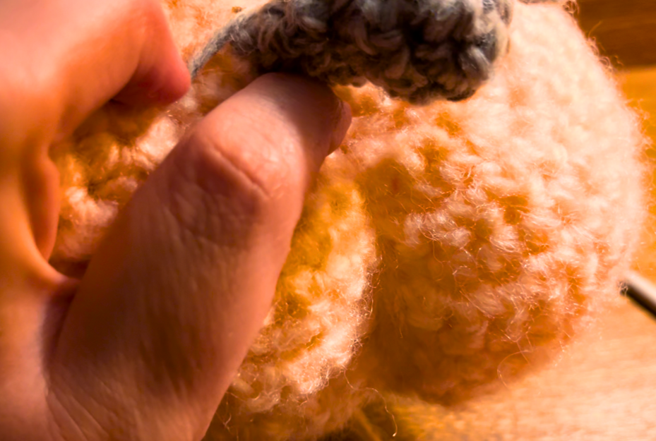 Woman pulling the yarn tight to make the side grooves of the crochet pumpkin