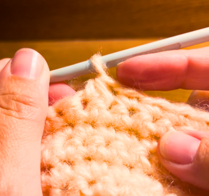 Woman crocheting with peach yarn and a grey hook