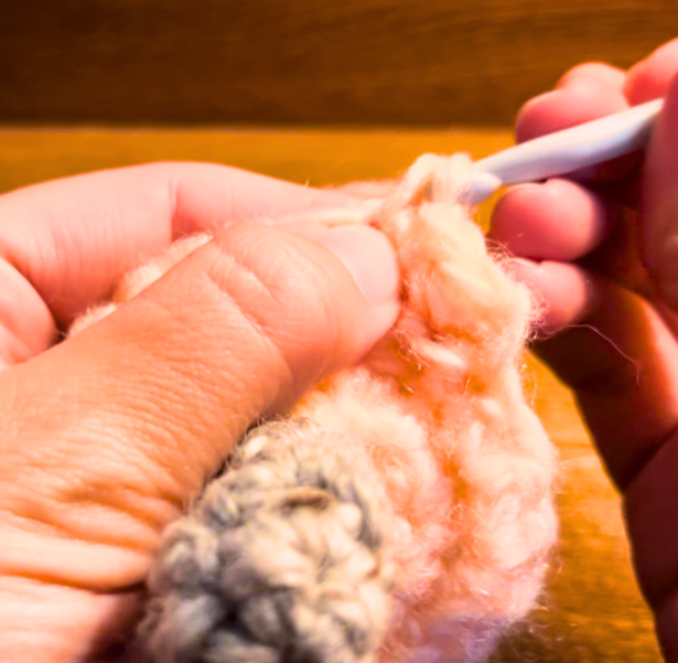 Woman crocheting with peach yarn and a grey crochet hook