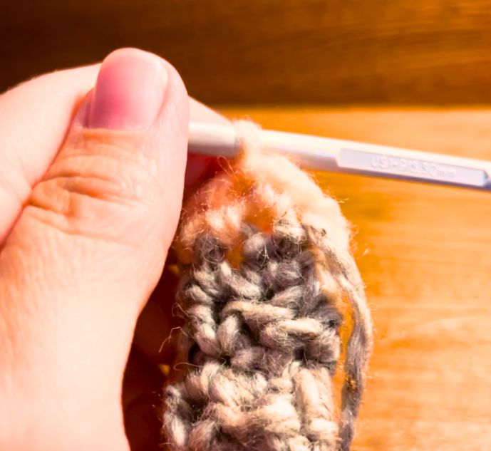 Woman switching from grey to peach yarn with a grey crochet hook