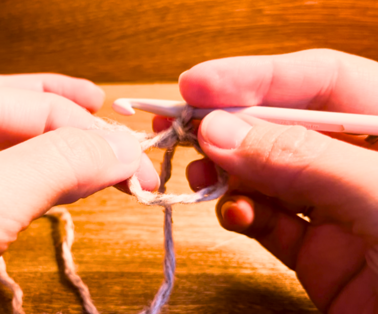 Woman holding a circle of grey yarn and a grey crochet hook
