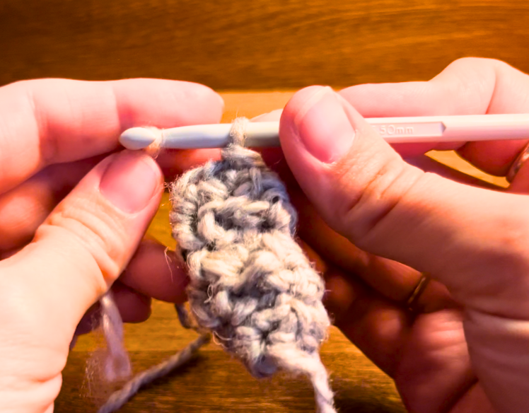 Woman crocheting with grey yarn and a grey hook