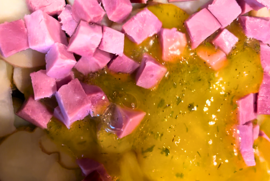 Pouring an egg mixture into a skillet with sliced potatoes and cubed ham.