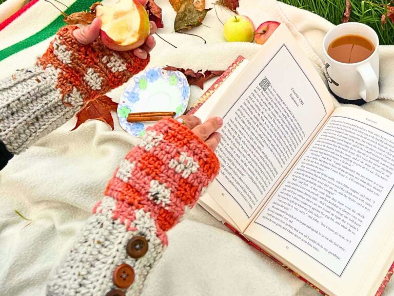 A woman is wearing orange and grey fingerless gloves. She is holding an apple that has be partially eaten. She is turn the page of a book.