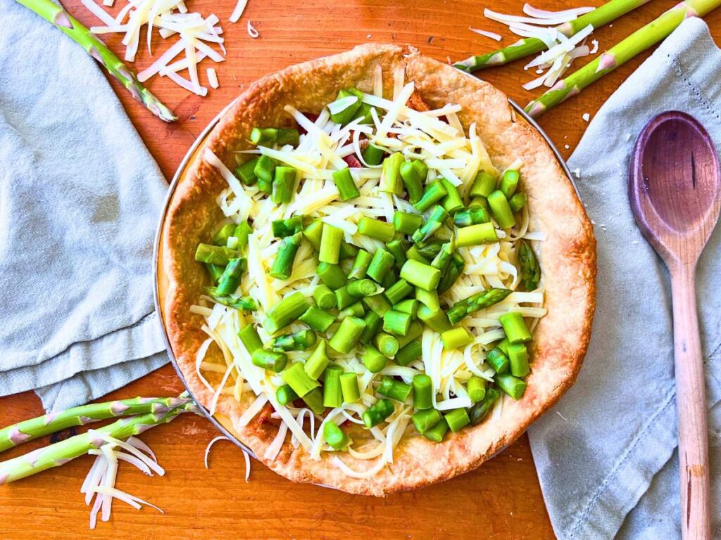 A baked pie crust with bacon, grated cheese, and asparagus inside.