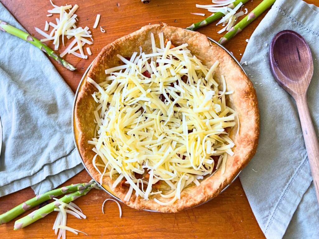 A baked pie crust with bacon and grated cheese inside.