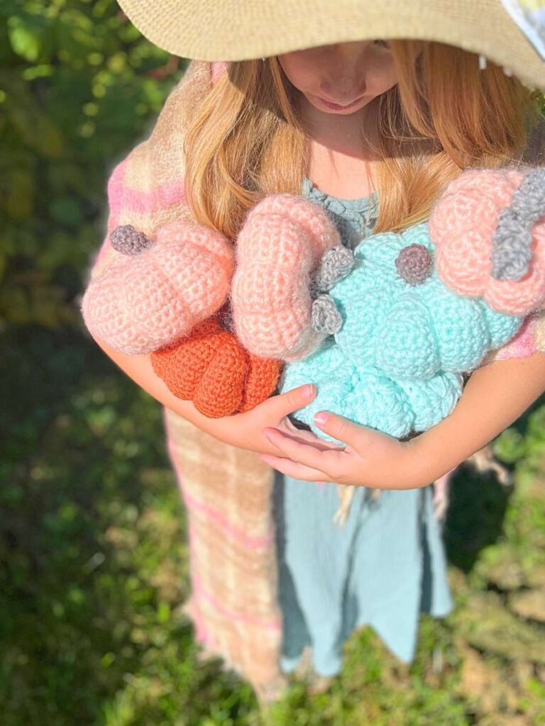 There is a girl holding a collection of crochet pumpkins.