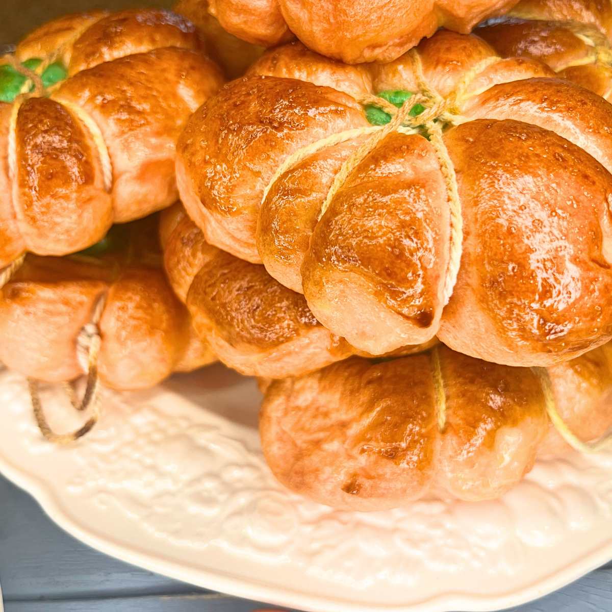 There is a plate full of pumpkin shaped bagels with kitchen twine wrapped around them.