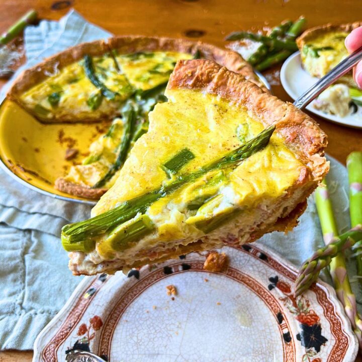 A woman is holding a slice of asparagus quiche.