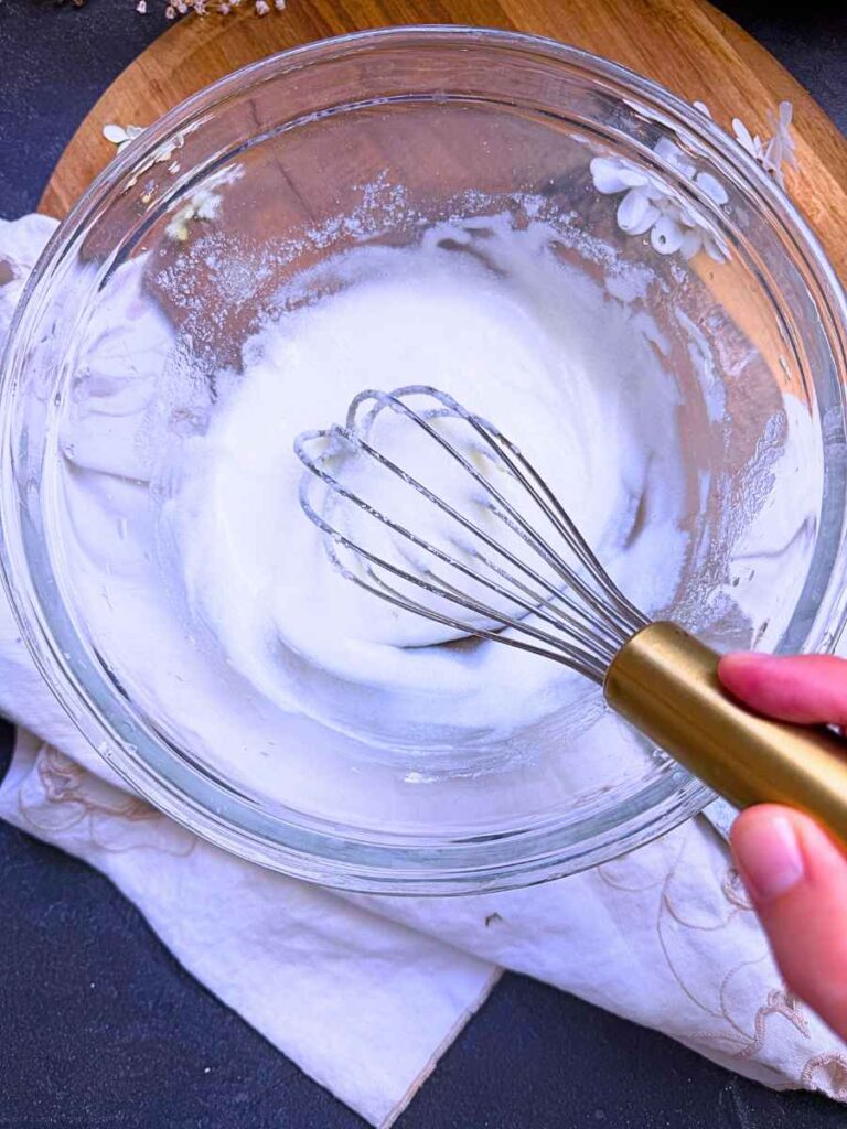 A woman is whisking vanilla glaze in a glass bowl.