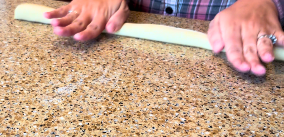 Woman rolling bread dough in to long cylinders on a brown countertop.
