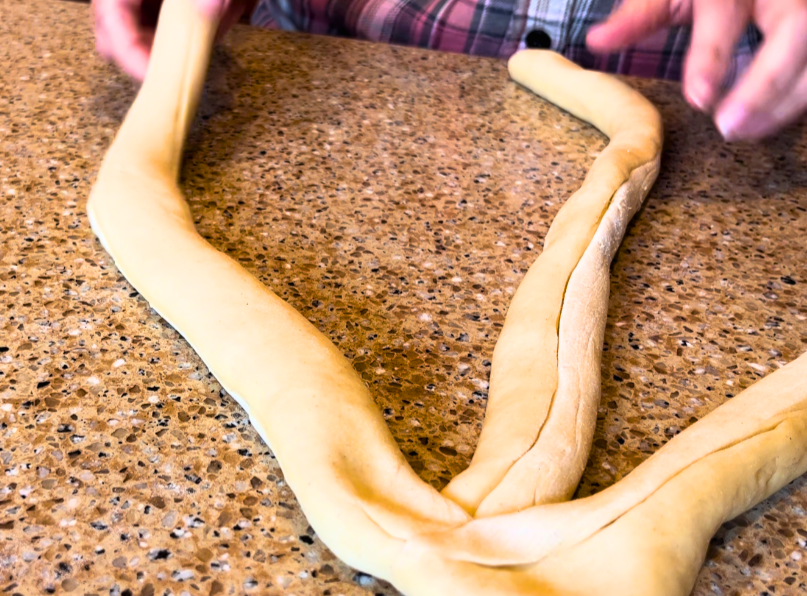 Woman pinching 3 strips of dough together to start a braid.