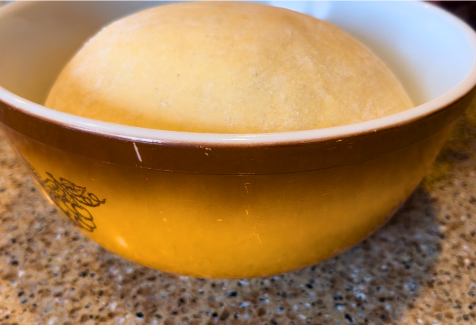 Risen bread dough inside a brown bowl on a brown countertop.