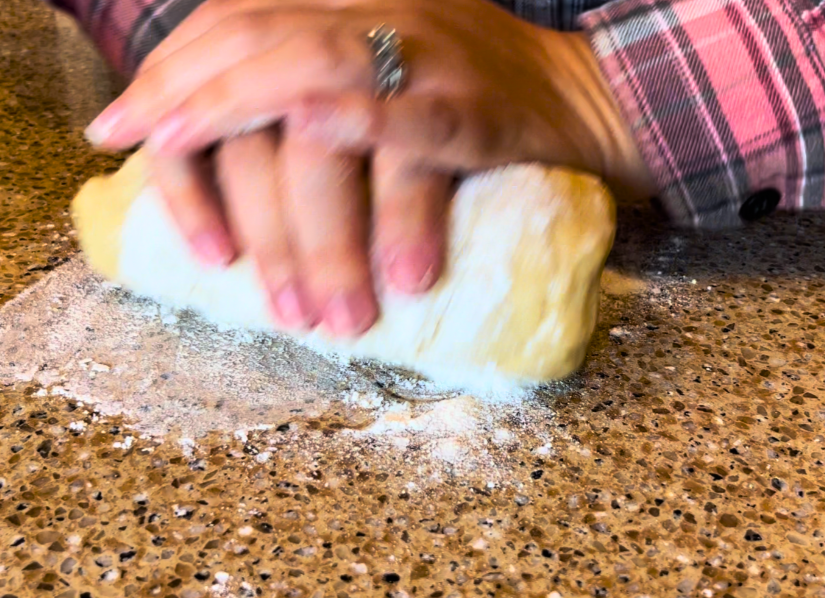 Woman kneading bread dough on a brown countertop.