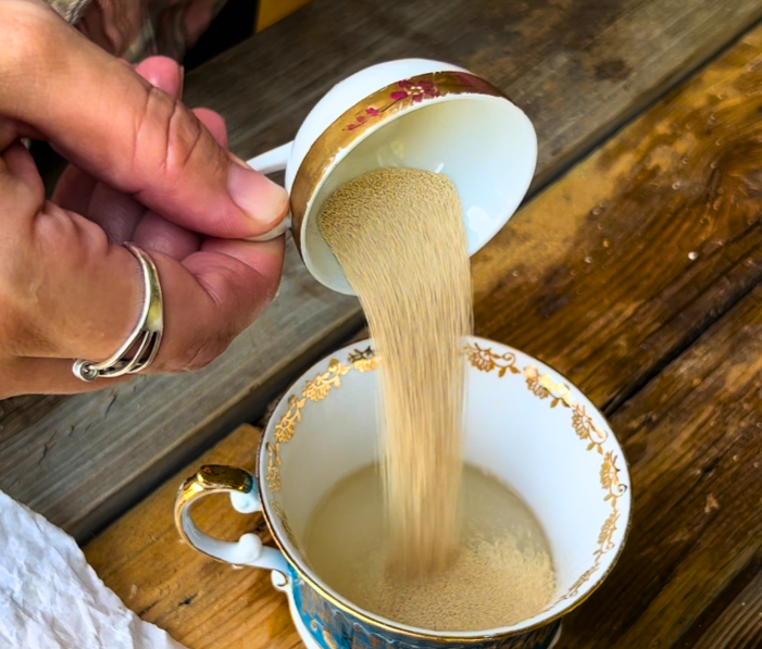 Woman pouring yeast into a cup of sugar and water.