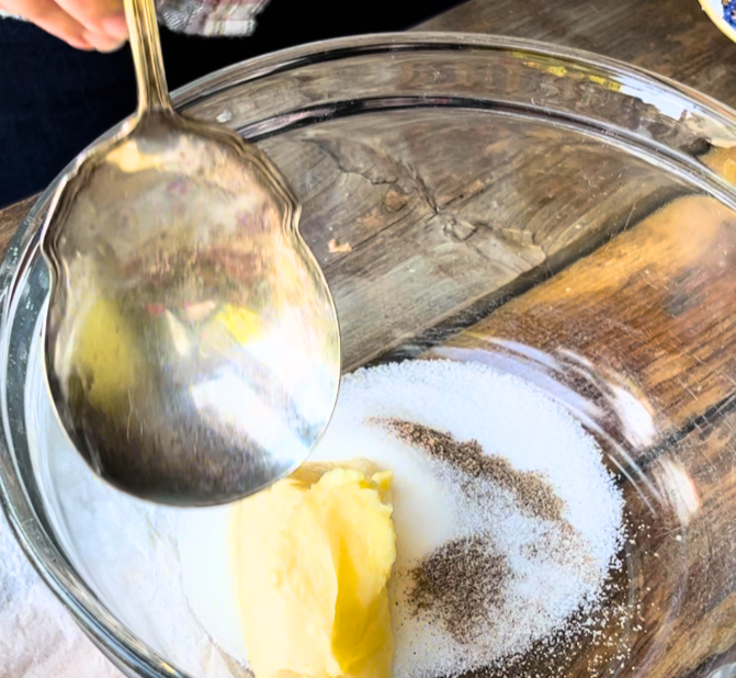 Woman mixing sugar, butter, salt, and cardamom in a glass bowl with a metal spoon.
