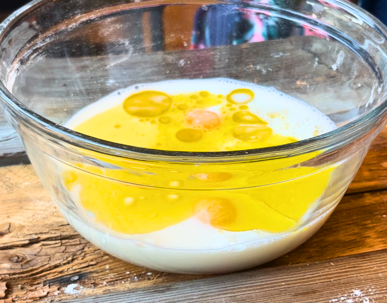 A glass bowl with milk, egg yolks, and oil.
