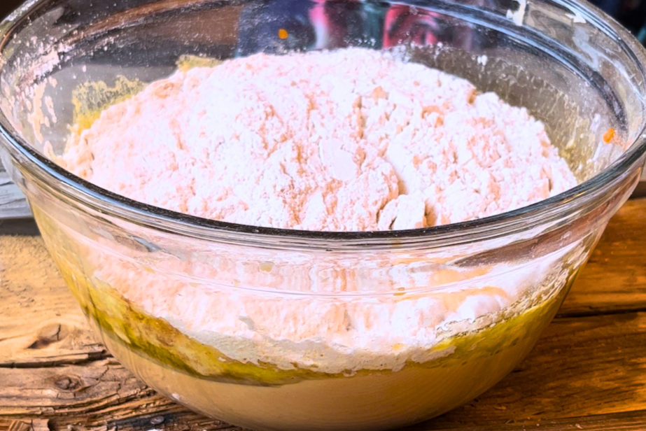 A glass bowl with orange batter at the bottom and a flour mixture at the top.