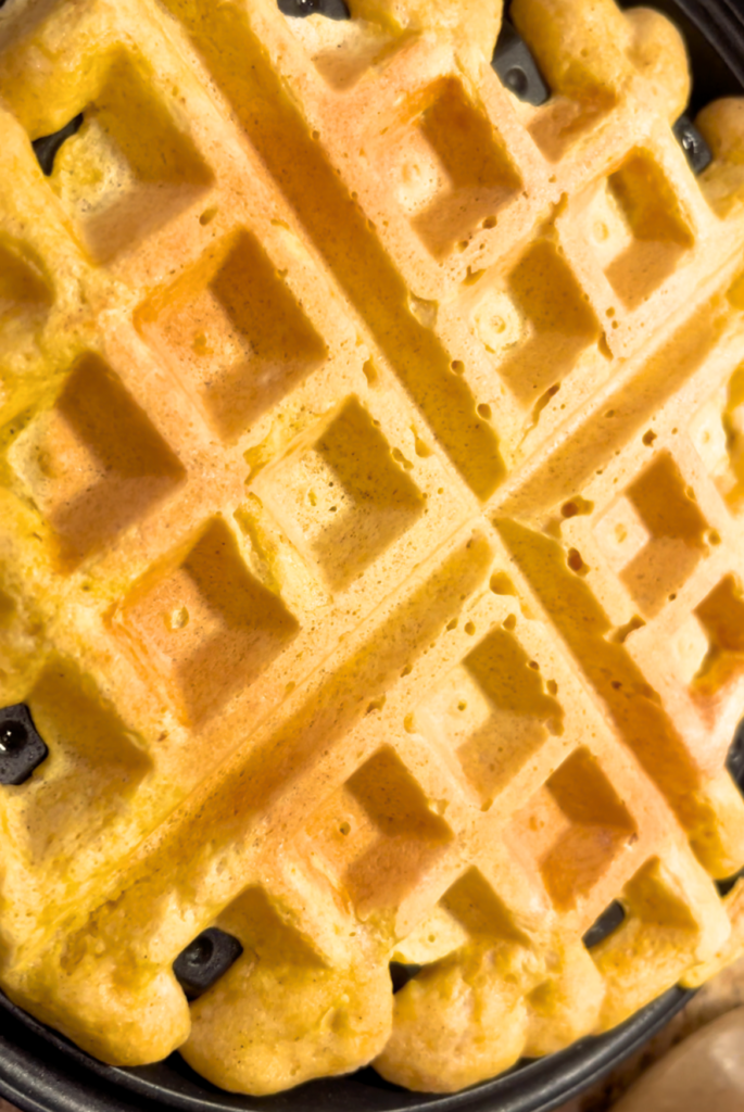 A cooked waffle on a black waffle iron.