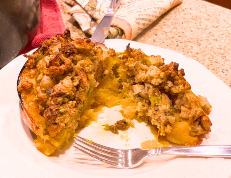 A cut, cooked, apple stuffed acorn squash. On a white plate with a metal fork