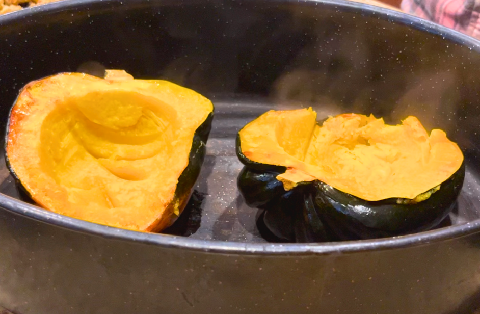 Cooked acorn squash in a black roasting pan.