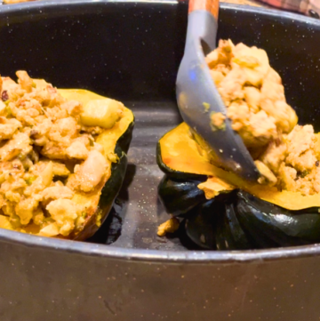 Woman spooning apple stuffing into cooked acorn squash halves, in a black roasting pan.