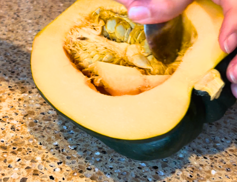 Woman scooping out the seeds of an acorn squash with a metal spoon.