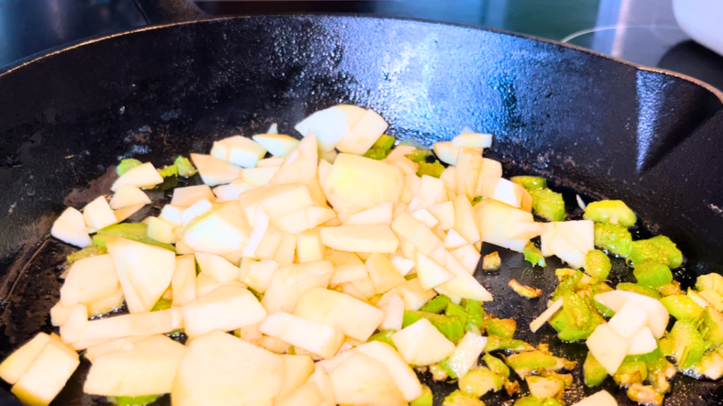 Adding apples to the celery in the cast iron skillet.