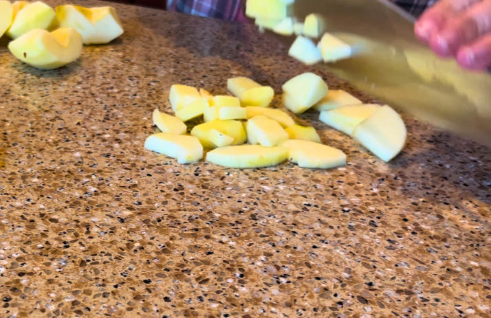 Woman chopping apples with a kitchen knife, on a brown countertop.