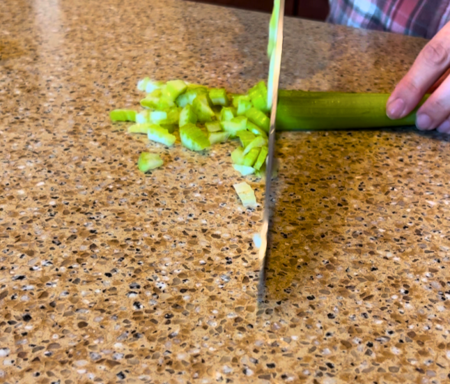Woman chopping celery with a metal kitchen knife on a brown countertop.