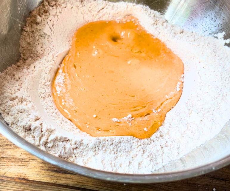 A metal bowl with flour mixture and a pumpkin mixture on top.