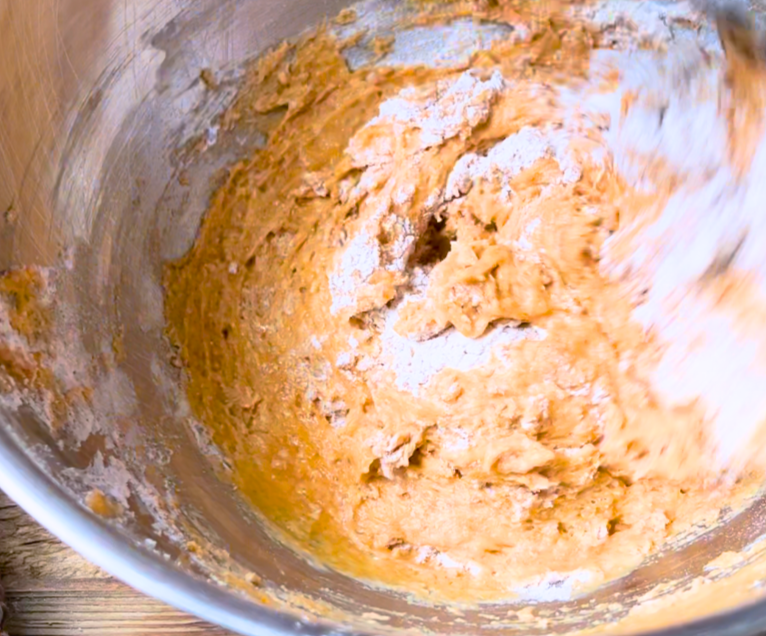 A metal bowl with pumpkin muffin batter being stirred.