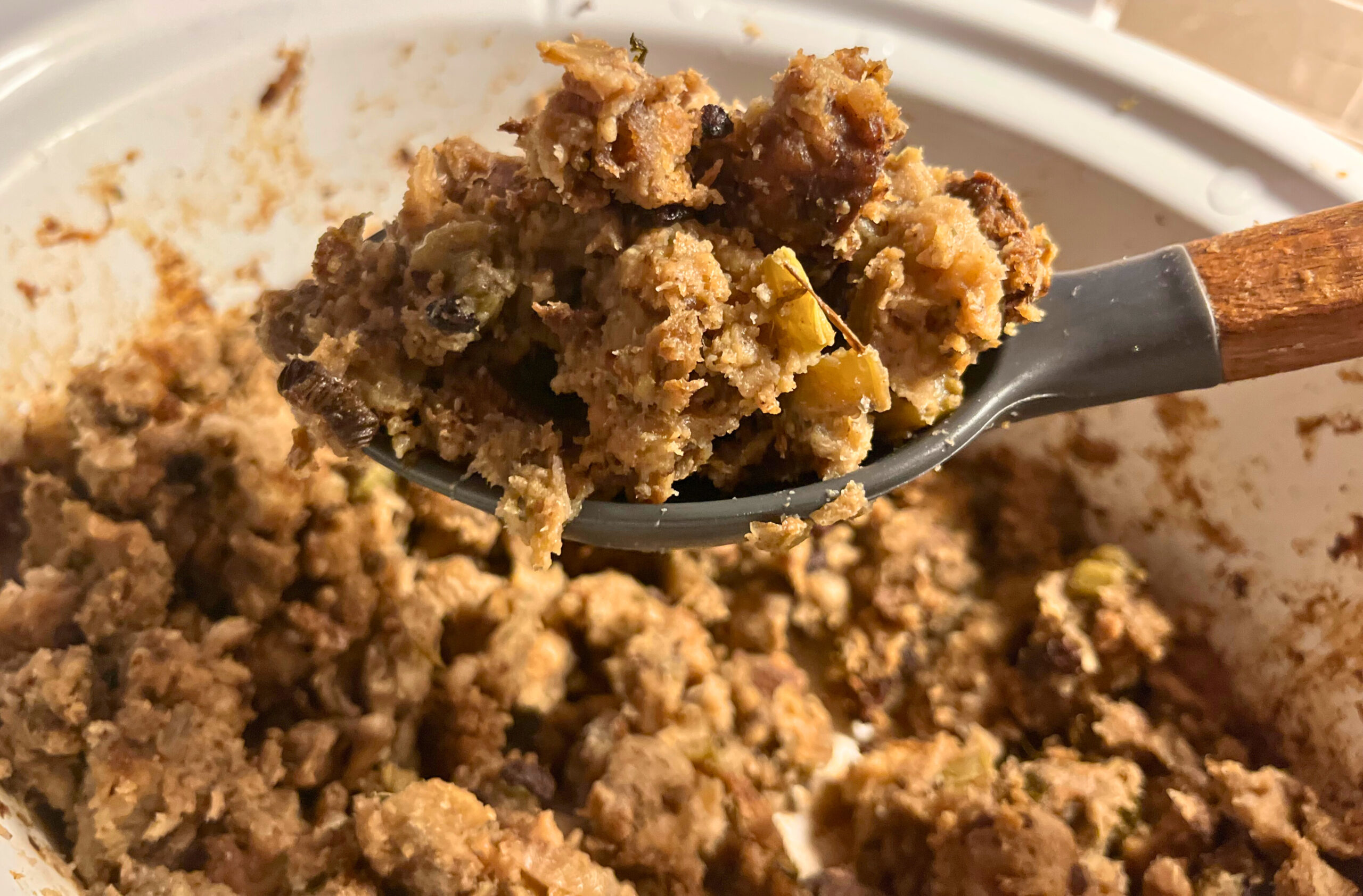 A wooden spoon with a scoop of cooked stuffing, overtop of a crockpot full of crockpot herb stuffing