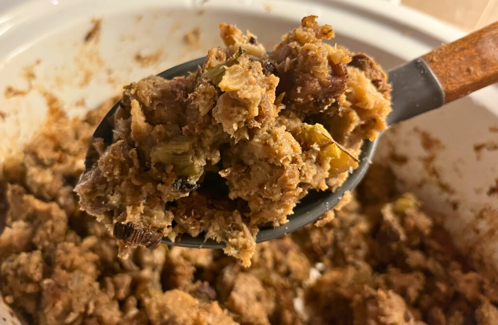 A wooden spoon with a scoop of cooked stuffing, overtop of a crockpot full of cooked herb crockpot stuffing