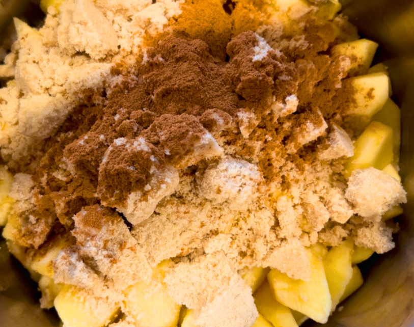 A large bowl of sliced apples with brown sugar, cornstarch, and cinnamon on top.