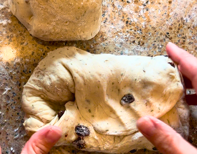 A woman folding herb stuffing bread dough.